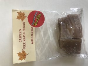 Small plastic bag of candy shaped like a cabin, with paper header that reads "Casper's Pure Maple Sugar" and a red sticker reading "Something Special from Wisconsin"